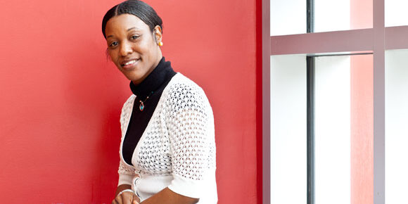 Smiling woman seated by a red wall.