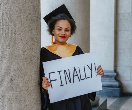 A woman in graduation cap and gown holding up a sign.