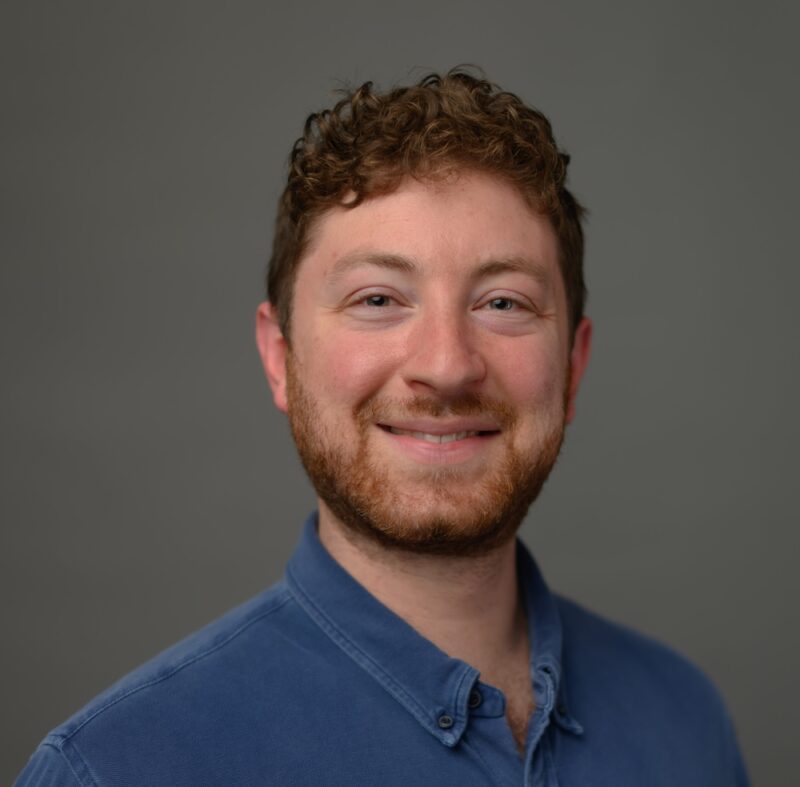 A man with a beard and blue shirt smiling.