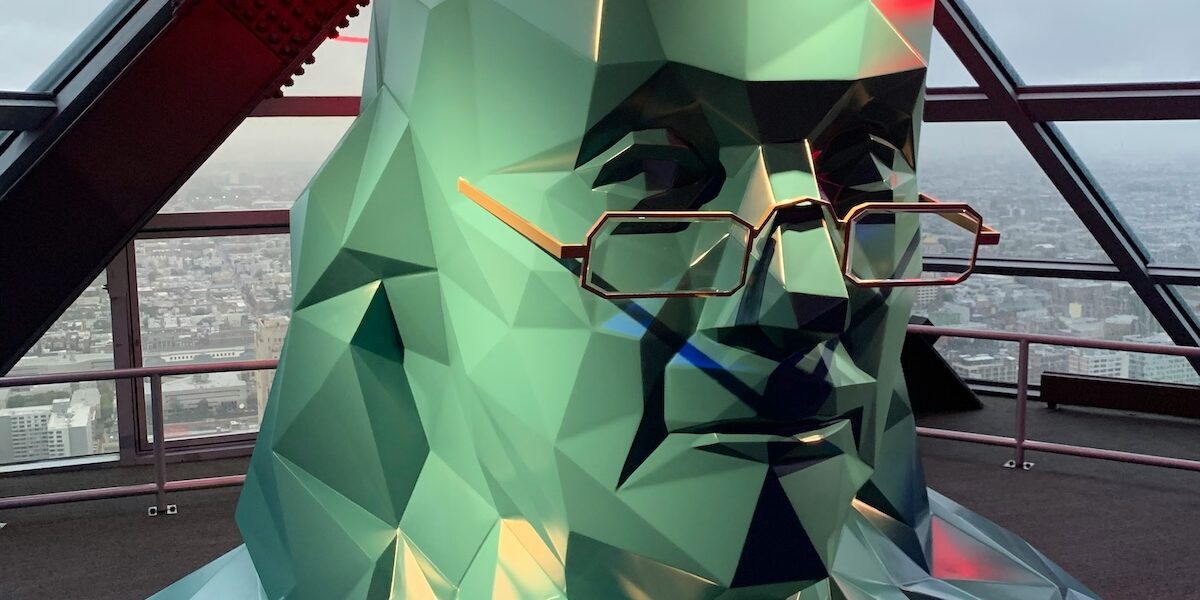 A green statue of ben franklin with glasses on it.