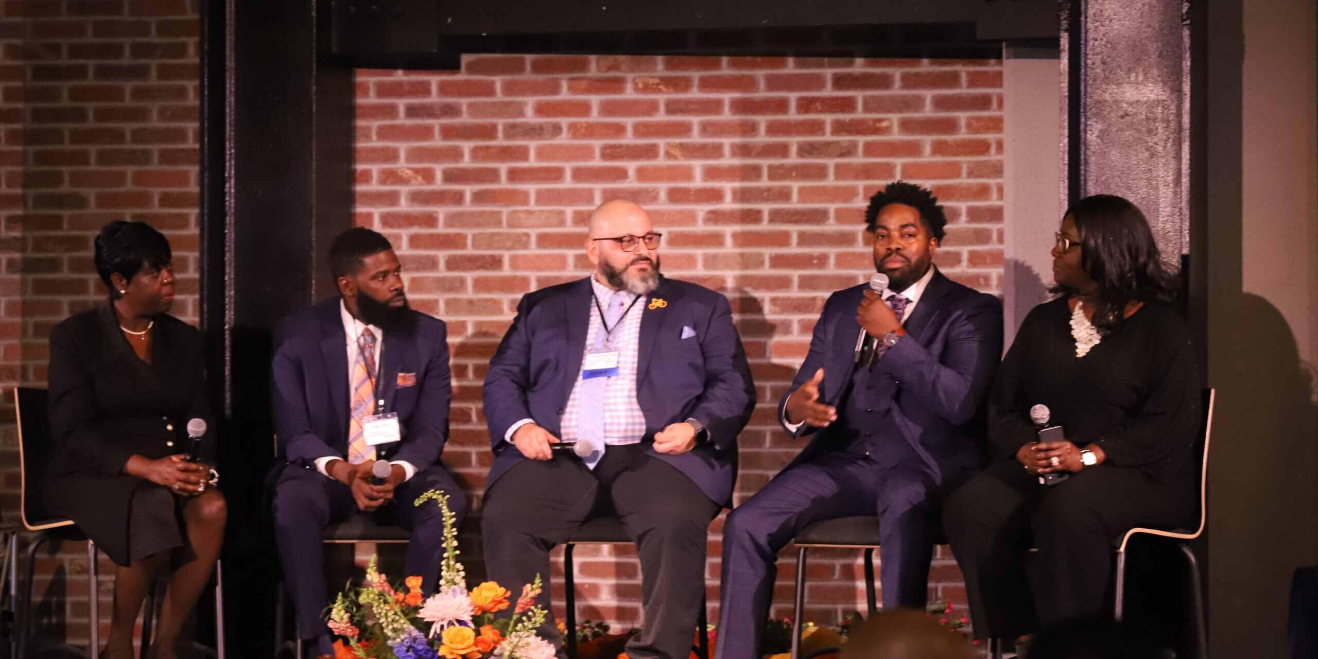 Four men in suits and ties sitting on chairs.